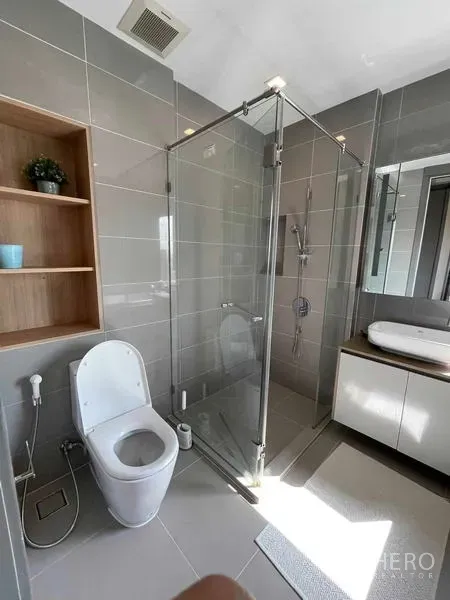 Condominium for rent or sale in Bang Rak, Bangkok - Modern bathroom featuring a glass shower enclosure, wall-mounted vanity, and open wooden shelving.