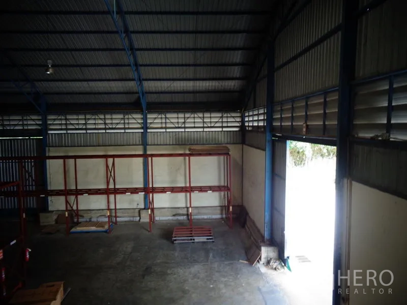 货栈 出租或出售在Lat Lum Kaeo, Pathum Thani - 角落区域，卷帘门开启，墙体百叶通风口与空置货架。