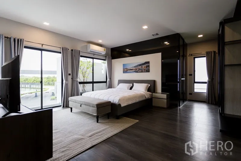 Townhouse for rent in Samut Prakan - Spacious master bedroom with floor-to-ceiling windows, wood floors and TV.