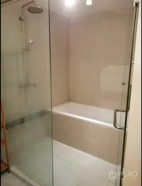 Condominium for rent in Khlong Toei, Bangkok - Bathroom with glass-enclosed shower next to a built-in bathtub.