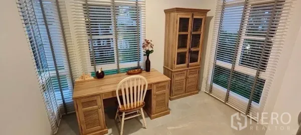 Detached House for rent in Prawet, Bangkok - Bright corner study with large windows, blinds, wooden desk, and display cabinet.