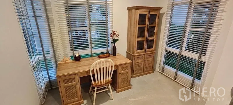 Detached House for rent in Prawet, Bangkok - Bright corner study with large windows, blinds, wooden desk, and display cabinet.