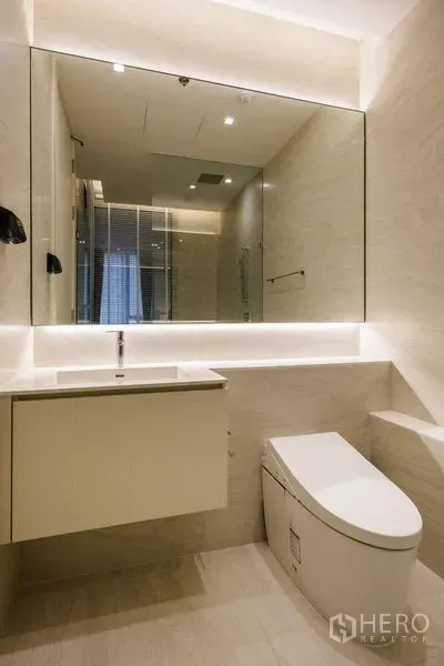 Condominium for rent in Watthana, Bangkok - Modern beige bathroom with backlit mirror, floating vanity, smart toilet and glass shower.