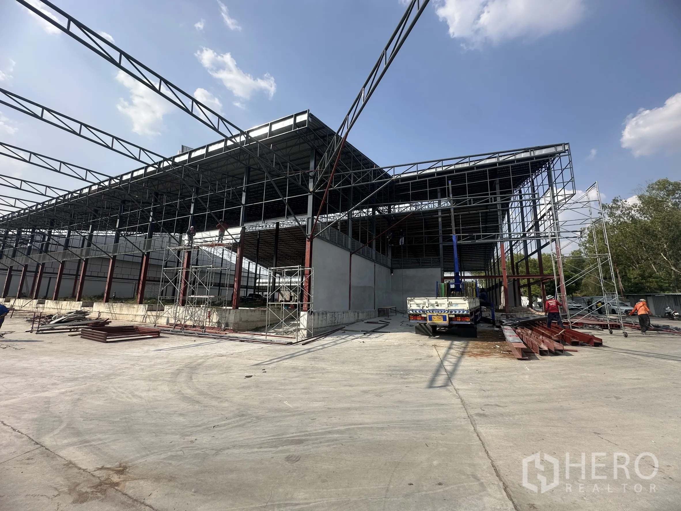 工厂 for rent in Si Racha, Chon Buri - 厂房结构配有脚手架与卡车，前方为大面积混凝土场地。