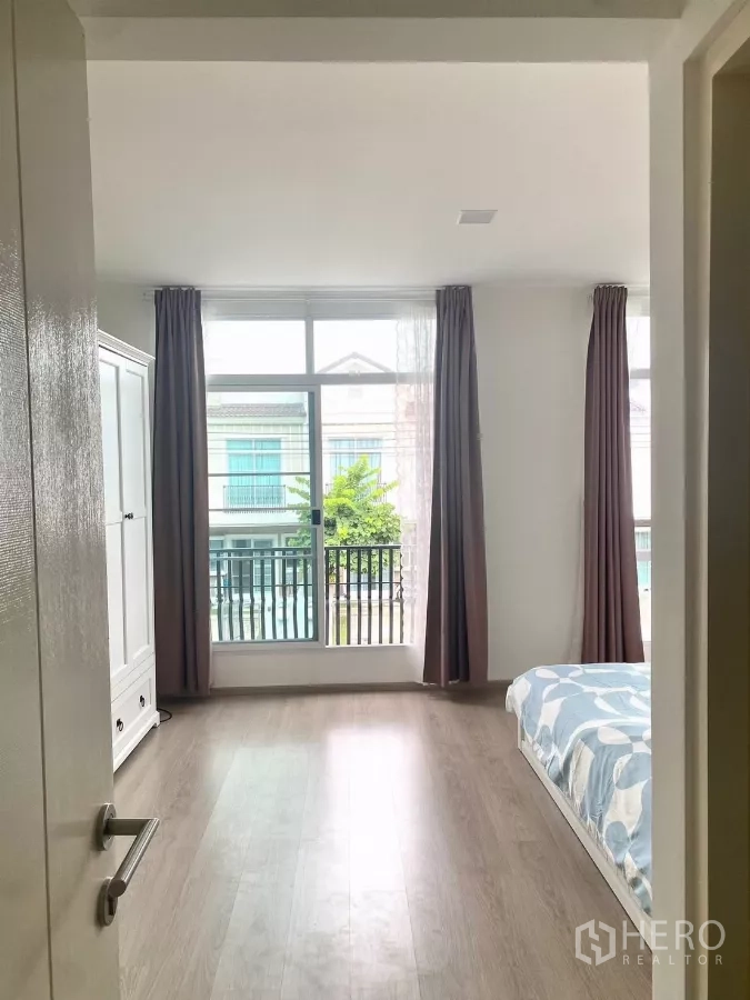 联排别墅 出租在Prawet, Bangkok - 卧室入口，落地窗与窗帘可见。