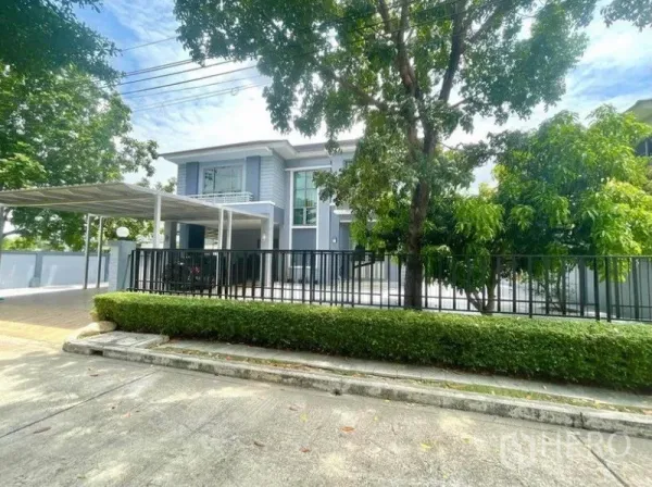 独立式住宅 出租在Prawet, Bangkok - 街景角落地块，黑色围栏、成树与宽阔车道。