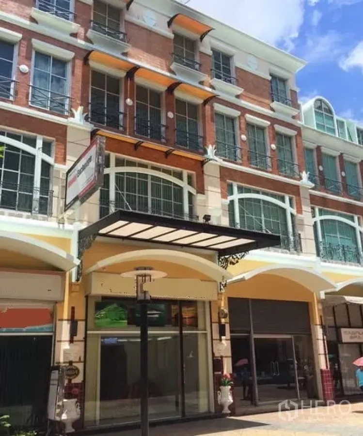 带办公室的家 出租或出售在Pathum Wan, Bangkok - 多层店屋风格外立面，红砖与米色拱廊，带阳台，蓝天下的建筑外观。