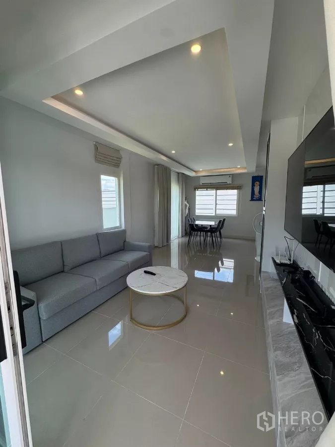 Detached House for rent in Bang Phli, Samut Prakan - Bright living room with gray sofa, marble coffee table, TV wall and adjoining dining area.