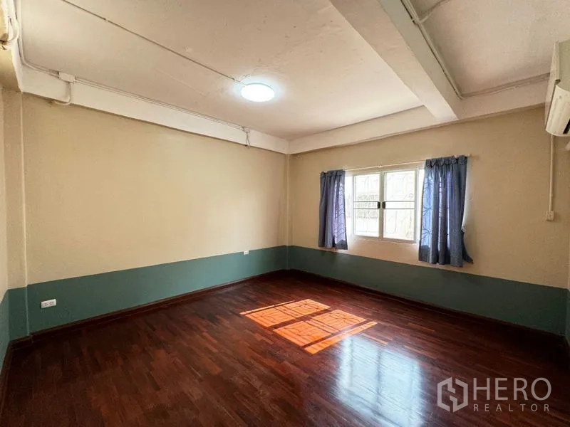 Townhouse for rent or sale in Suan Luang, Bangkok - Sunlit bedroom with wooden floor, window curtains and wall air conditioner