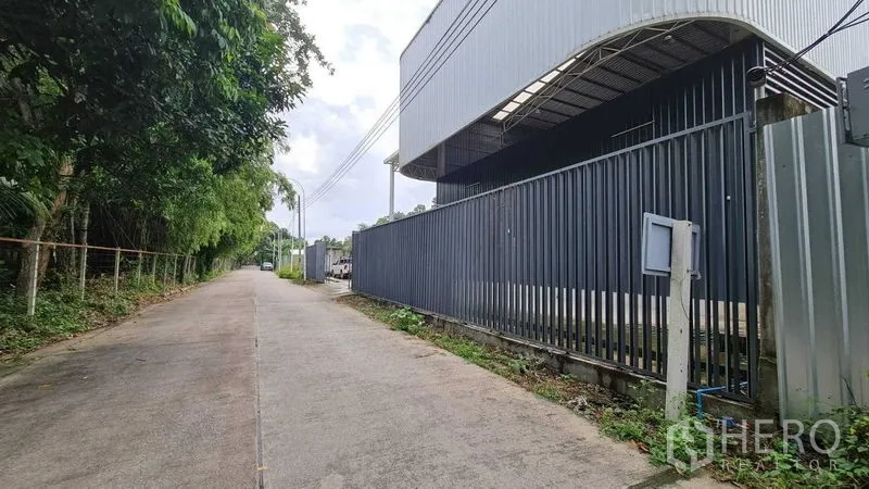 Warehouse for rent in Mueang Nonthaburi, Nonthaburi - Quiet lane beside the warehouse with a tall metal fence and overhead utility lines.