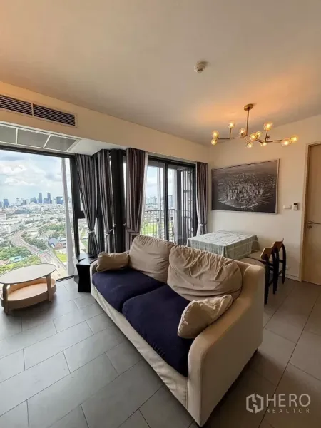 公寓 出租或出售在Phaya Thai, Bangkok - 采光充足的客厅，沙发与餐桌、枝形吊灯，落地窗通向阳台，可眺望曼谷天际线。