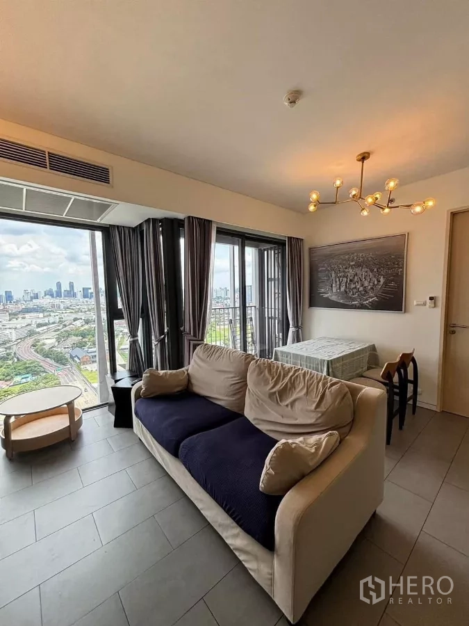 Condominium for rent or sale in Phaya Thai, Bangkok - Bright living room with sofa, dining table, chandelier, and floor‑to‑ceiling windows opening to a balcony with Bangkok city views.