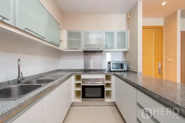 Condominium for rent in Khlong Toei, Bangkok - U-shaped modern kitchen with granite countertops, oven, microwave, and glass-front cabinets.