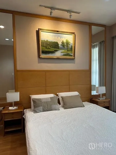 Condominium for rent in Khlong Toei, Bangkok - Master bedroom with king bed, twin side tables, soft lighting and framed landscape art on wood paneling.