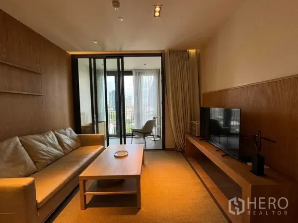 Condominium for rent in Khlong Toei, Bangkok - Living area opening to a balcony with city views through floor-to-ceiling glass.