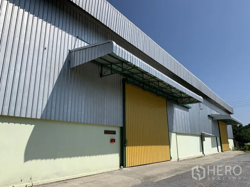 货栈 出租在Lat Krabang, Bangkok - 金属板外立面的仓库，黄色大滑门与装卸雨棚，蓝天下的外观。