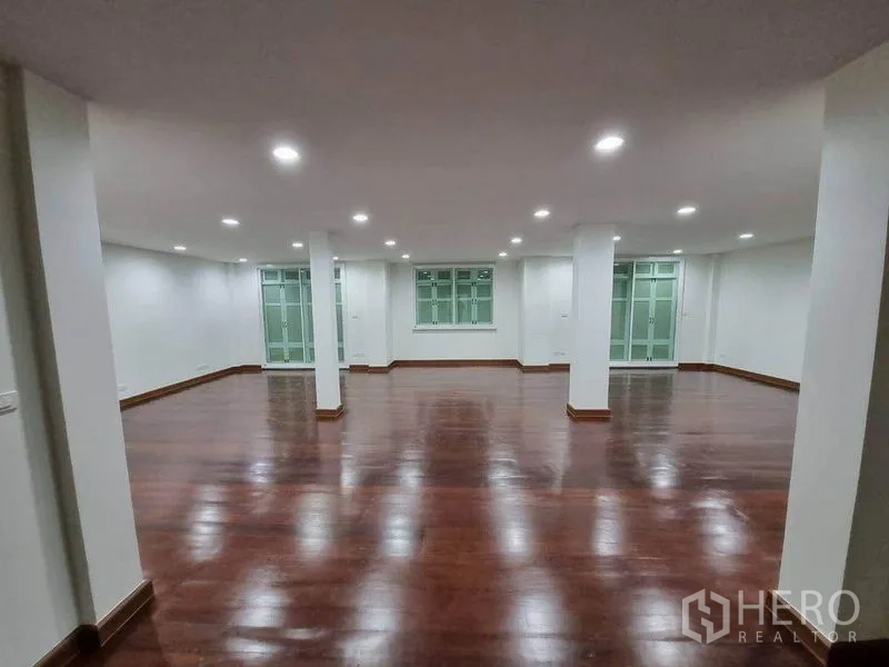店屋 出租在Bang Rak, Bangkok - 宽敞开放式楼层，深色木地板、白墙、筒灯与立柱，配大窗。