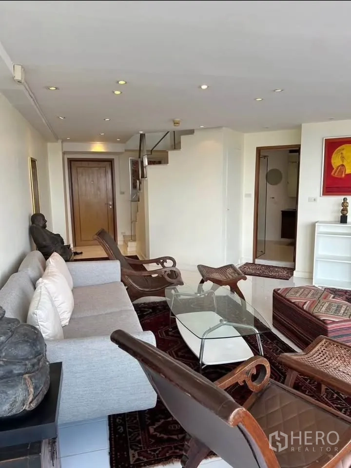 公寓 出租或出售在Yan Nawa, Bangkok - 温馨客厅，沙发、木椅、玻璃茶几与通往上层的楼梯。