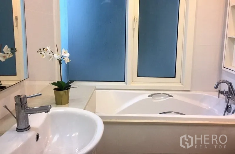 Condominium for rent in Khlong Toei, Bangkok - Bathroom with bathtub, vanity sink, mirror and frosted window.