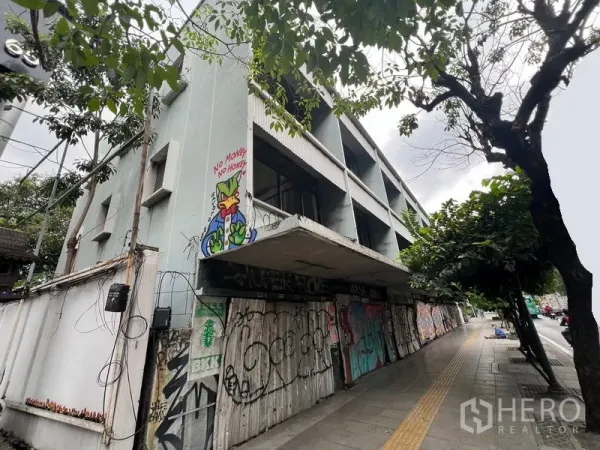 Land for rent in Watthana, Bangkok - Corner view of a shuttered building beside a tree-lined pavement.