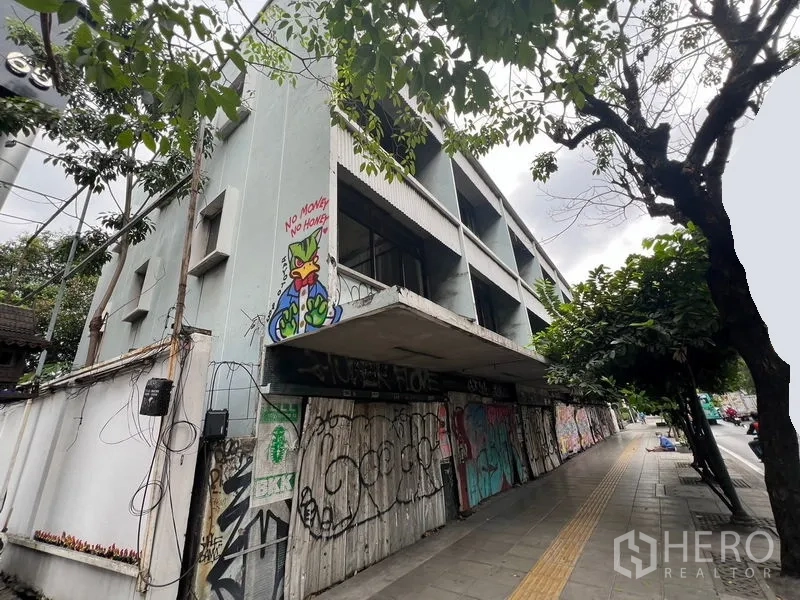 Land for rent in Watthana, Bangkok - Corner view of a shuttered building beside a tree-lined pavement.