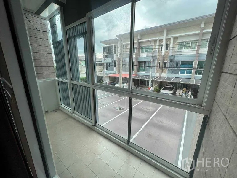 Townhouse for rent in Bueng Kum, Bangkok - Enclosed balcony with floor-to-ceiling windows overlooking townhomes and parking.