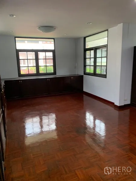 Detached House for rent in Khlong Toei, Bangkok - Bright living room with polished parquet flooring, dark built-in cabinets and large windows in a detached house near On Nut BTS.
