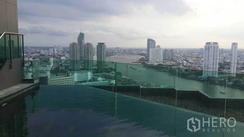 Condominium for rent in Sathon, Bangkok - Rooftop infinity pool with glass railing overlooking the Chao Phraya River skyline.