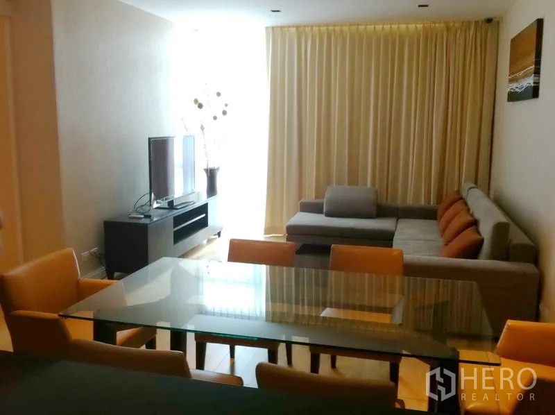公寓 出租在Pathum Wan, Bangkok - 开放式客餐厅，玻璃餐桌、L 型沙发、电视柜与落地窗帘。