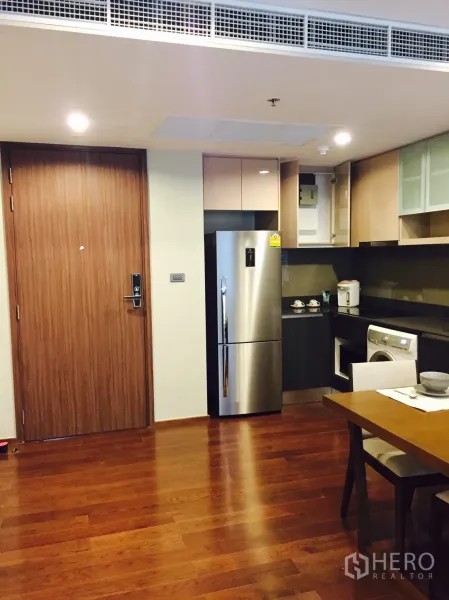 Condominium for rent or sale in Sathon, Bangkok - Open-plan kitchen and dining area with wooden flooring, built-in cabinets, stainless refrigerator, and washing machine.