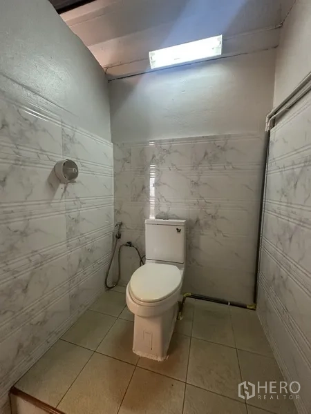 Shophouse for rent or sale in Phra Khanong, Bangkok - Compact bathroom with marble-look wall tiles, toilet, and natural light from skylight.