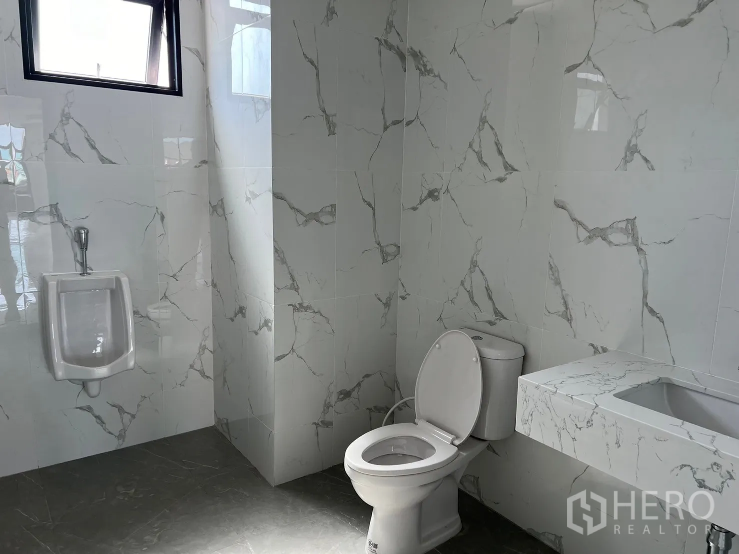 Warehouse for rent in Samut Prakan - Restroom finished in marble-pattern tiles with toilet, urinal and integrated counter.