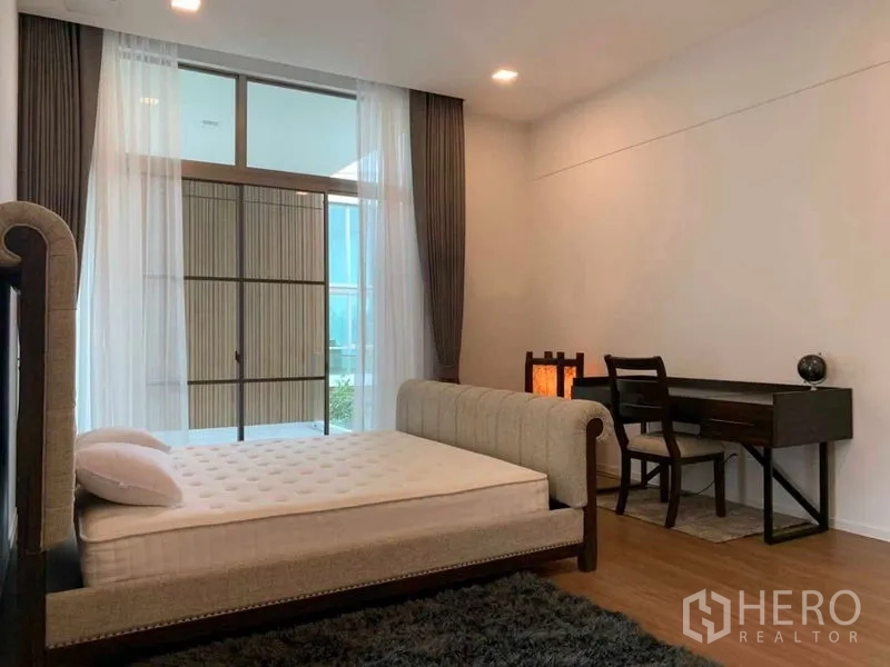 独立式住宅 出租在Saphan Sung, Bangkok - 大开间卧室带书桌区，落地窗与柔和灯光。