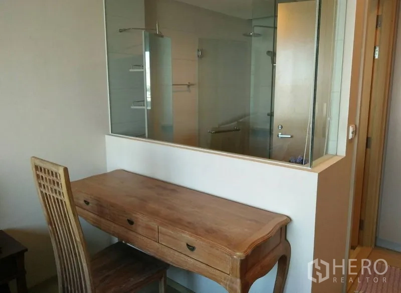 Condominium for rent in Khlong Toei, Bangkok - Wooden work desk facing a glass partition to a modern bathroom with glass-enclosed shower.