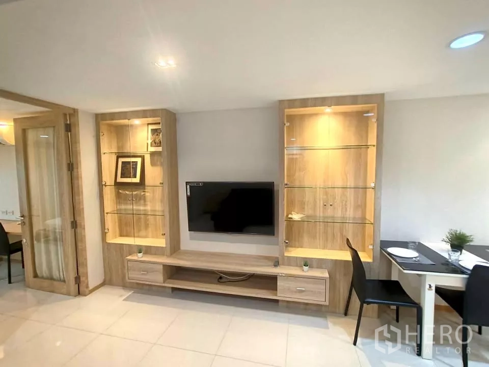 Condominium for rent in Khlong Toei, Bangkok - Built-in media wall with illuminated glass display shelves and a mounted TV beside a compact dining nook.