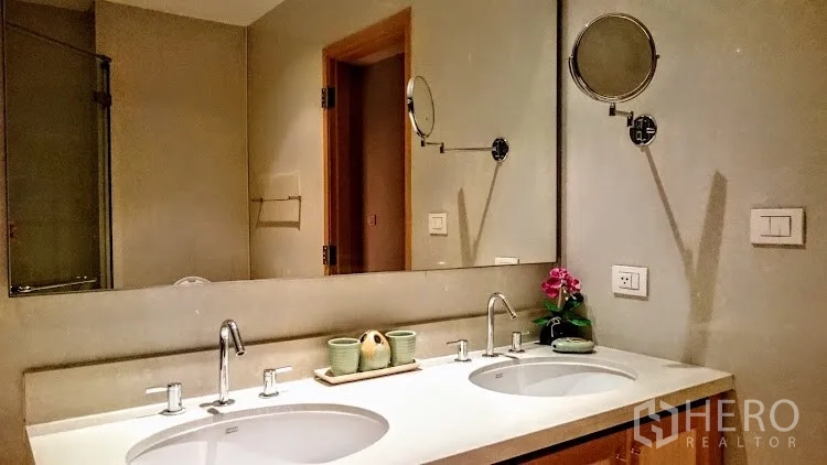Condominium for rent in Khlong Toei, Bangkok - Bathroom with double sinks, long mirror and glass-enclosed shower.