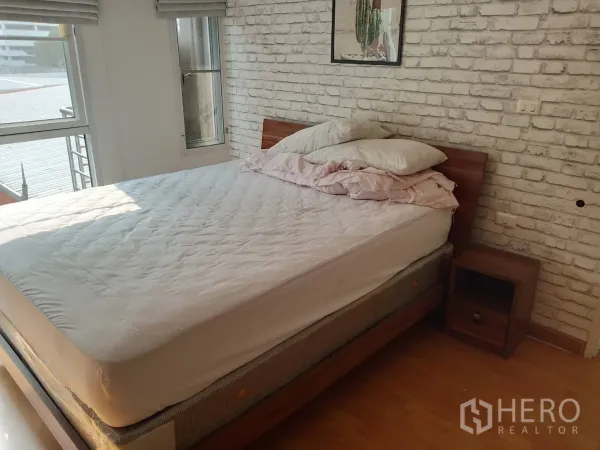 Condominium for rent or sale in Khlong Toei, Bangkok - Cozy bedroom with white brick accent wall, wooden bed and corner windows.