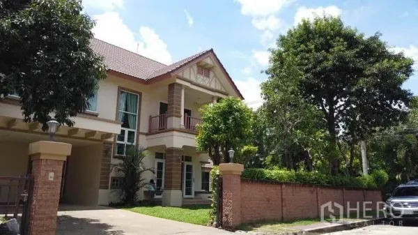 บ้าน ให้เช่าหรือขายในPak Kret, Nonthaburi - มุมมองหน้าบ้านสองชั้นหลังกำแพงอิฐ มีทางรถเข้าและต้นไม้ใหญ่
