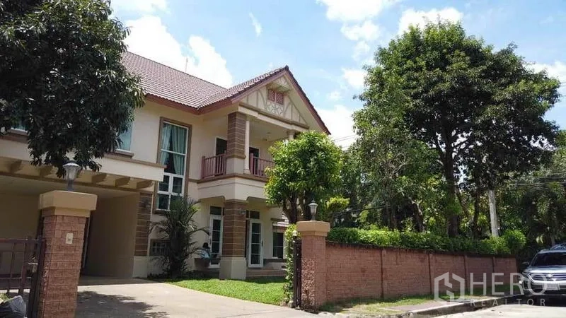 独立式住宅 出租或出售在Pak Kret, Nonthaburi - 街景视角的两层住宅，砖砌围墙、车道与绿树相映成趣。