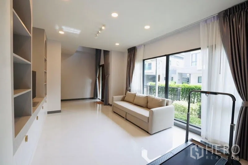 独立式住宅 出租在Bang Phli, Samut Prakan - 客厅设沙发与跑步机，落地窗通向花园景观。