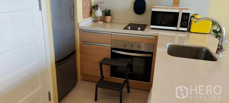 Condominium for rent or sale in Khlong Toei, Bangkok - Compact kitchen with built-in oven, electric cooktop and a tall refrigerator.