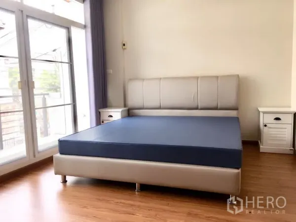 联排别墅 出租在Prawet, Bangkok - 主卧带大窗与阳台推拉门，两侧设床头柜。