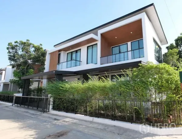 Detached House for rent or sale in Thanyaburi, Pathum Thani - Street view of corner detached house with landscaped hedges and balcony railings.