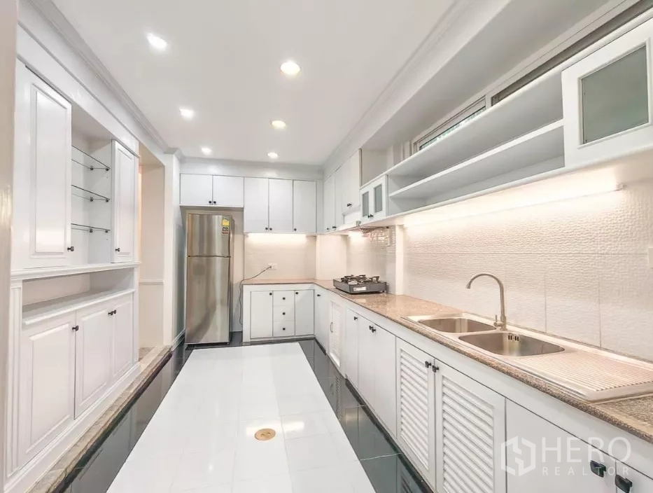 Detached House for rent in Yan Nawa, Bangkok - Modern galley kitchen with white cabinetry, double sink, gas cooktop, and stainless fridge.
