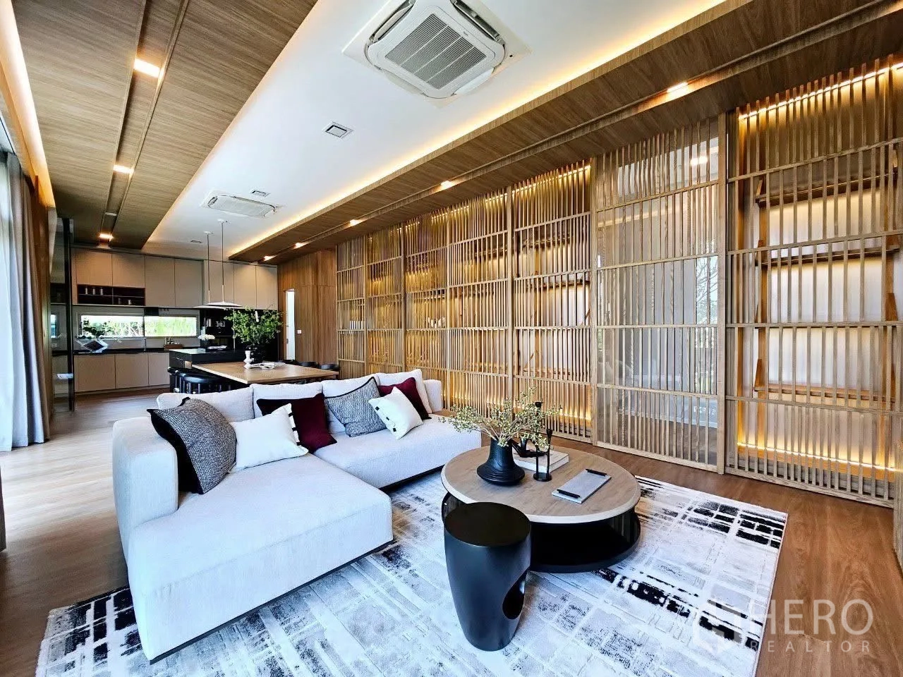 Detached House for rent in Saphan Sung, Bangkok - Open-plan living room with L-shaped sofa, wood slat feature wall, and island kitchen.