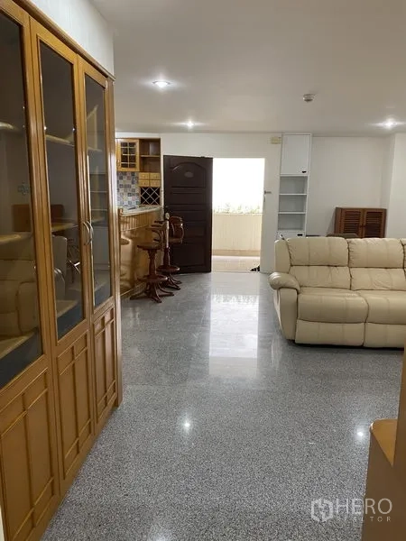Condominium for rent or sale in Watthana, Bangkok - Open-plan living area leading to the kitchen and balcony, featuring wood cabinetry, breakfast bar stools and glossy granite flooring.