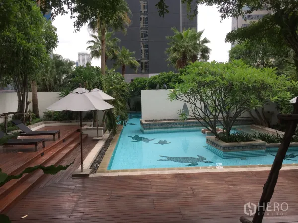 Condominium for rent in Pathum Wan, Bangkok - Resort-style outdoor swimming pool with wooden sun deck, loungers and lush tropical trees in a city condo.