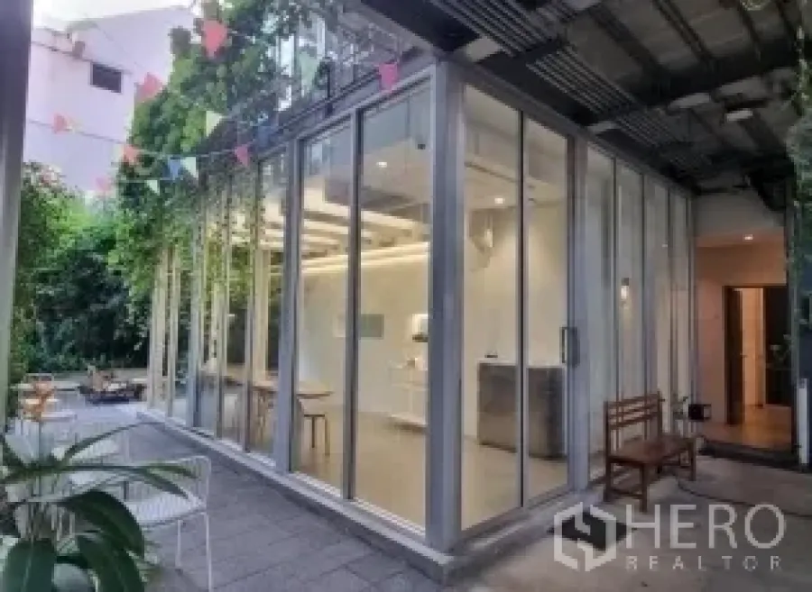 Retail Space for rent in Khlong Toei, Bangkok - Corner exterior of a glass-box retail unit with a covered patio, greenery, and outdoor seating.