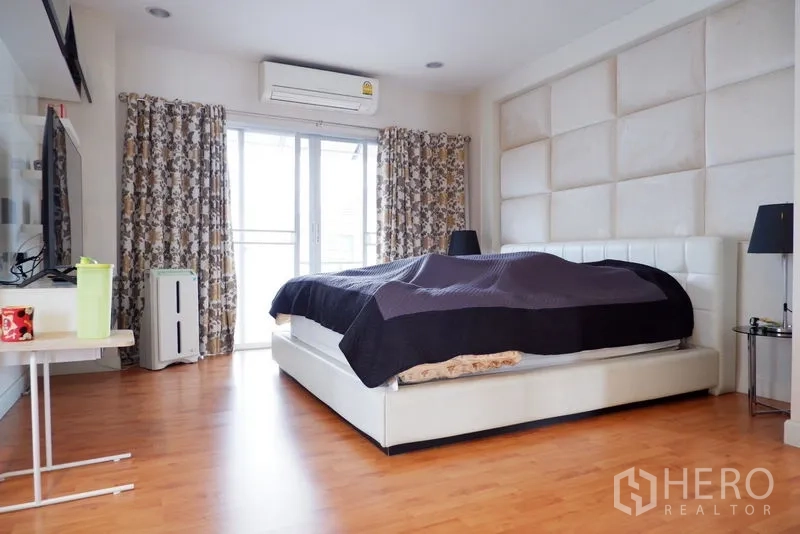 Detached House for sale in Saphan Sung, Bangkok - Master bedroom with padded headboard, balcony access and wood flooring.
