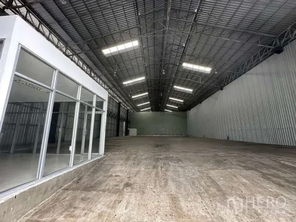 货栈 出租在Pak Kret, Nonthaburi - 高挑仓库大厅，照明充足，混凝土地面，侧边有办公室。